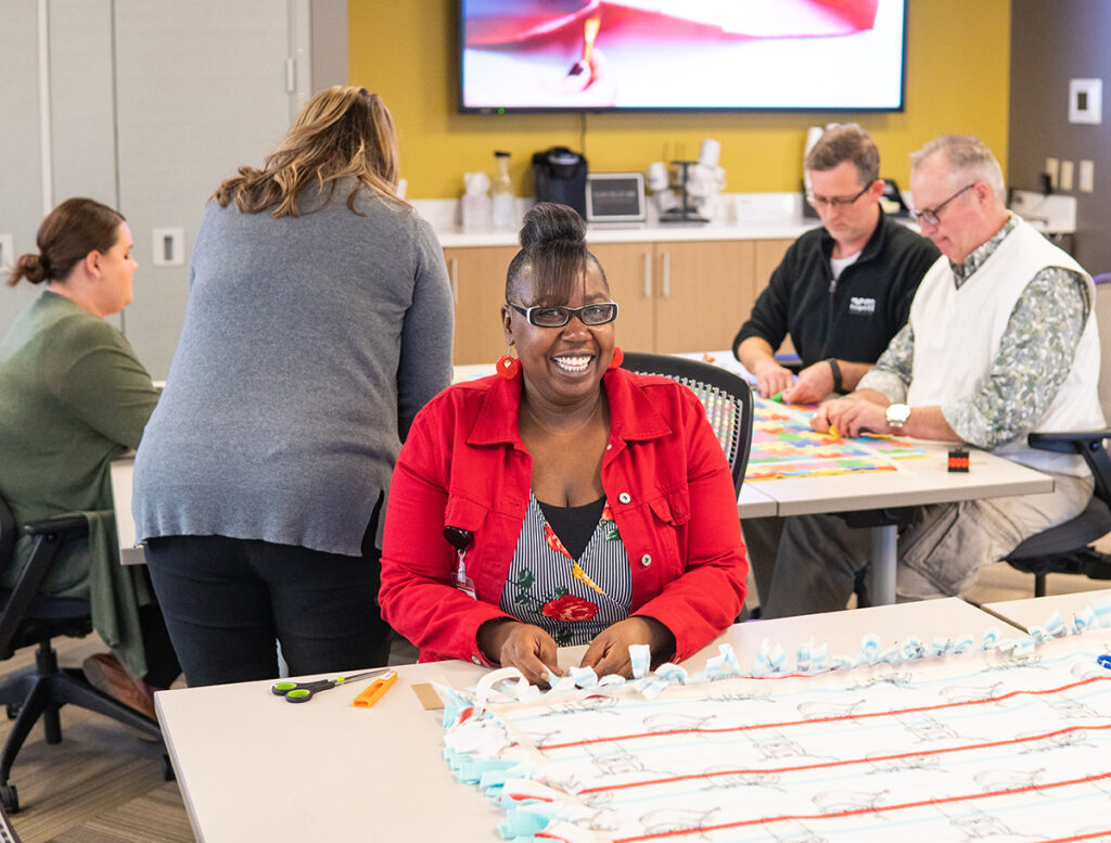 a woman is smiling while making a fleece blanket at a volunteer event in an office setting