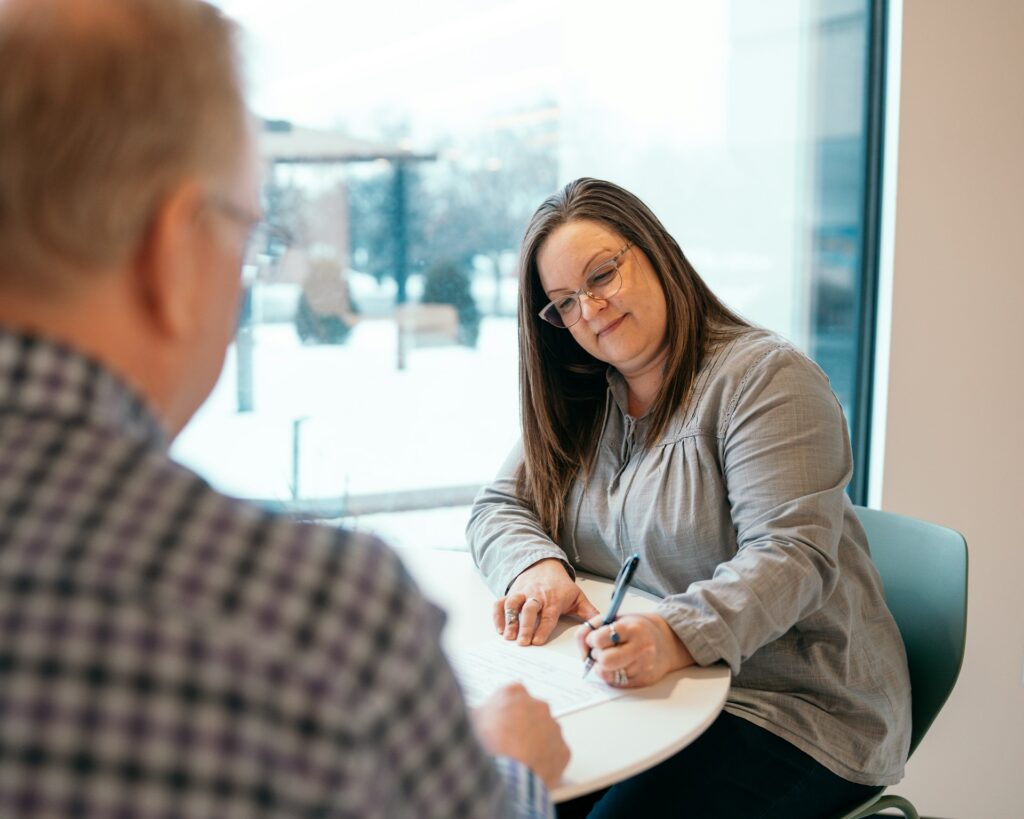 a man and woman are sitting at table. the woman is signing a document between them.