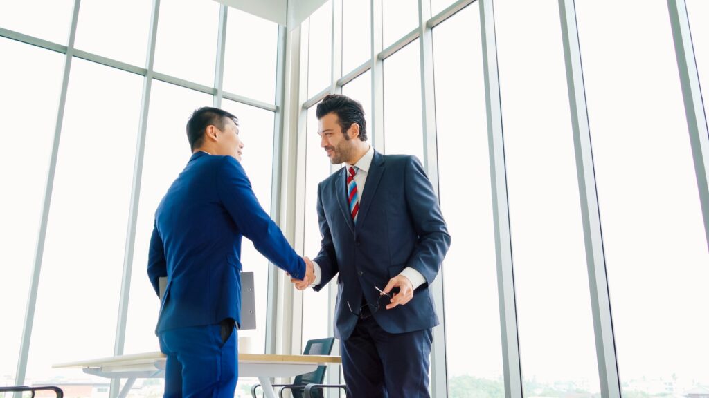 two men shake hands while smiling in an office setting