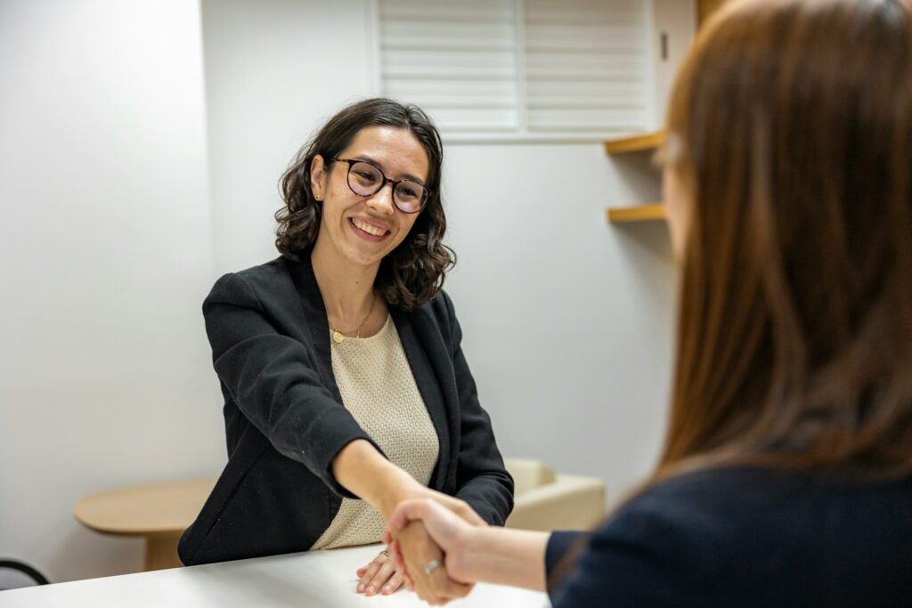 two women shake hands in an office setting.