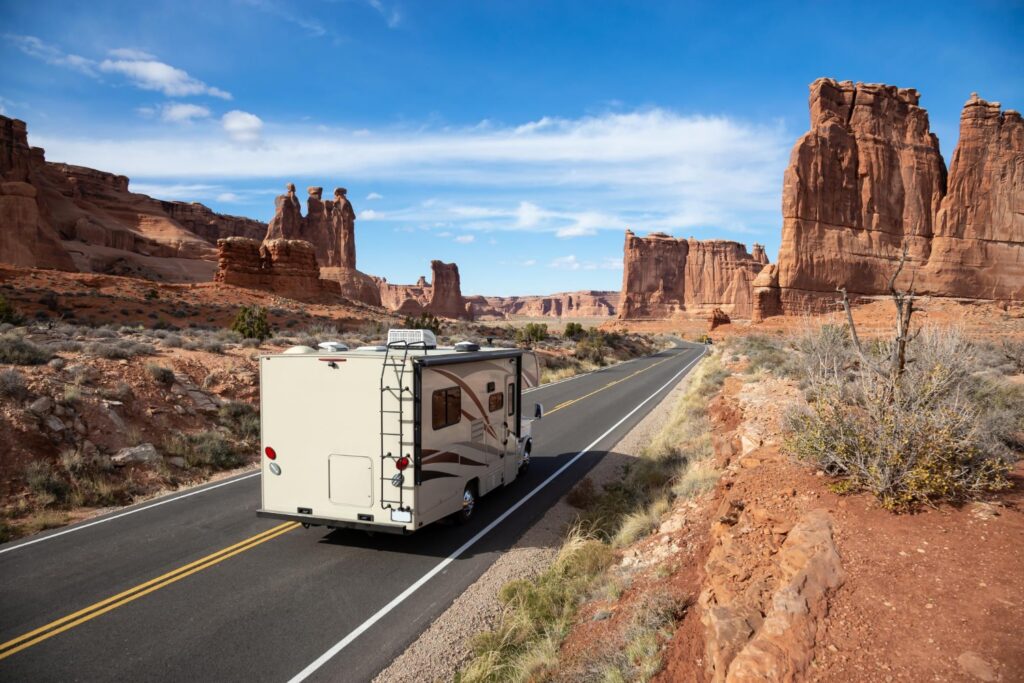 an RV trailer driving on a desert road surrounded by red rock formations under a blue sky