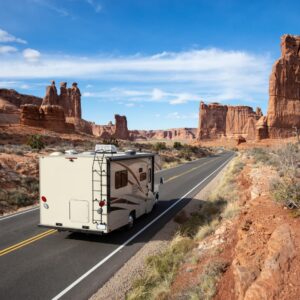 an RV trailer driving on a desert road surrounded by red rock formations under a blue sky
