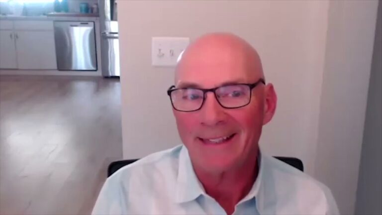 Alan Harvey, wearing glasses and a collared shirt, sits facing the camera and smiling during a powersports training session