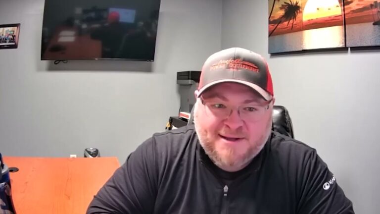 Brian Coulter, a man with glasses, a black shirt, and a ball cap, sits facing the camera