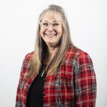 Crystal Cordoba wears a red jacket and glasses. She is smiling and facing the camera.