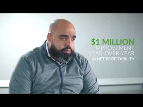 Jose Oliver, has shaved head and a full beard, wearing a grey jacket sits facing the camera, in the background it reads $1 million improvement year-over-year in net profitability