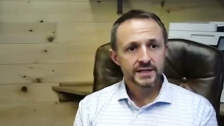 Lee Parish, a man in a striped collared shirt, sits in his desk chair facing the camera