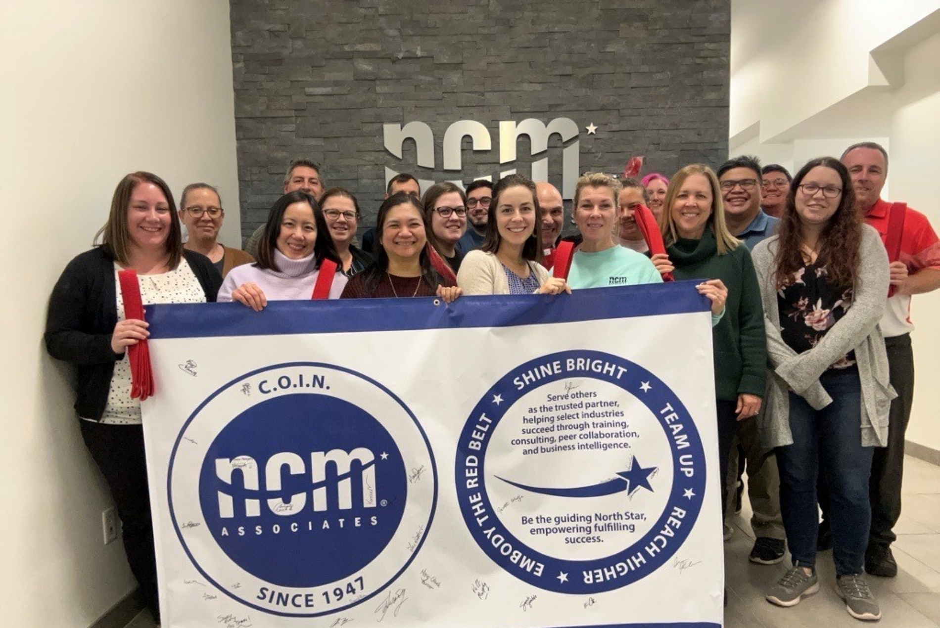 a photo of the NCM team holding a banner detailing the community values of the company